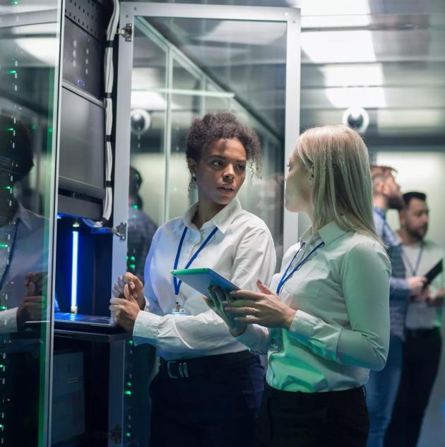 Medium shot of two women working in a data center with rows of server racks and checking the equipment and discussing their work