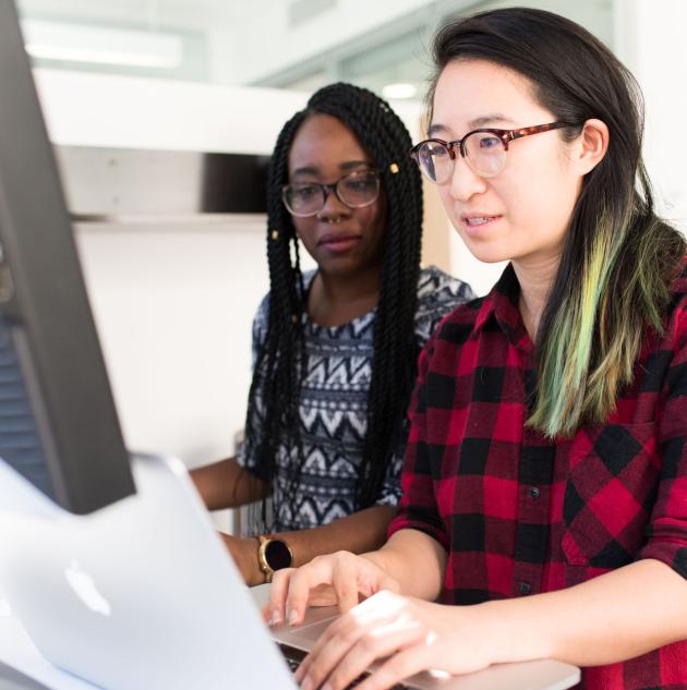 Two women use MacBook computer