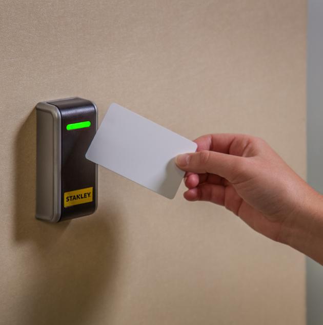 Hand holds key card up to smart lock mounted on wall.