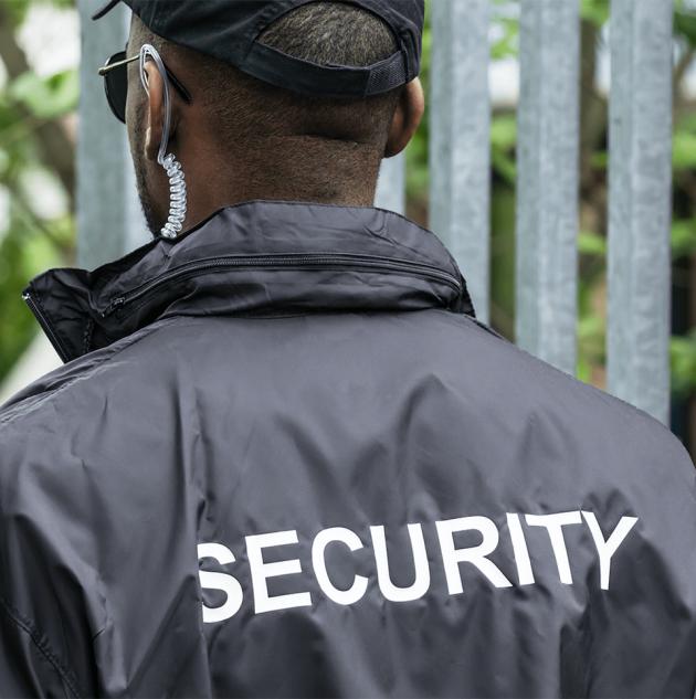 Security patrol guards stands near metal gate.