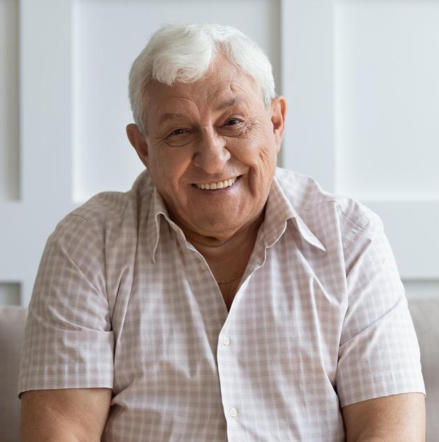 Smiling older man sits on sofa.