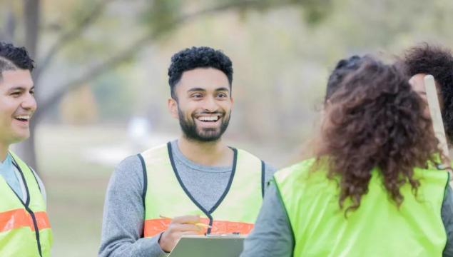 Confident young man talks with a group of male and female community volunteers. He is giving them instructions. They are wearing safety vests.