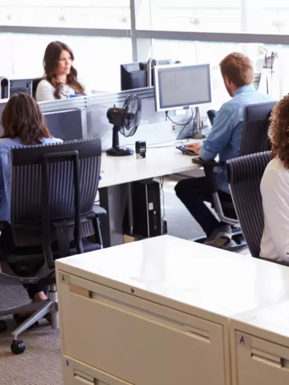 People in business attire sit in an open space workplace, talking on phones and working on their computers.