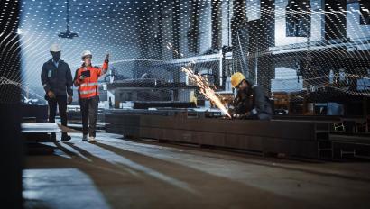 Two Heavy Industry Engineers Walk in Steel Factory, Use Tablet and Discuss Work. Industrial Worker Uses Angle Grinder in the Background. Black African American Specialist Talks to Female Technician.