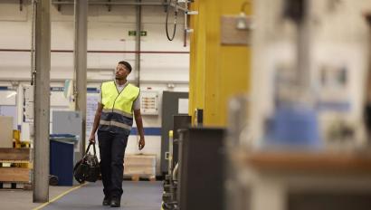 a technician wearing a safety vest walking through an industrial facility, representing Securitas Technology's commitment to on-site security service and maintenance