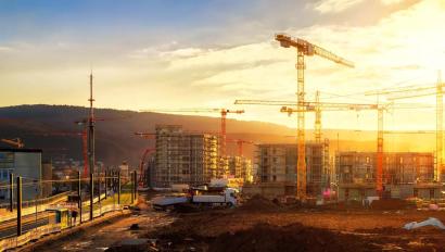 Large construction site including several cranes working on a building complex, illumined by warm gold sunlight
