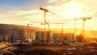 Large construction site including several cranes working on a building complex, illumined by warm gold sunlight