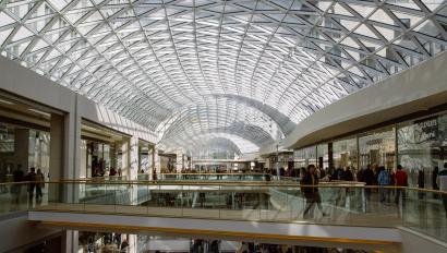 large multi-level shopping mall with various stores, escalators, and visible security measures, including a retail alarm system in place to protect the premises