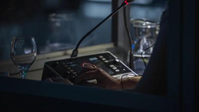 Translator or translation booth at a conference. Hand of a person for simultaneous translating is seen working in a booth. Glass of water next to a translator.