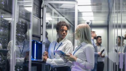 Medium shot of two women working in a data center with rows of server racks and checking the equipment and discussing their work