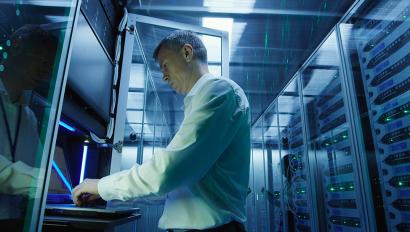 IT technician works at laptop in server room