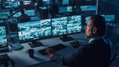 Male Officer Works on a Computer with Surveillance CCTV Video Footage