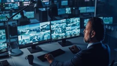 Male Officer Works on a Computer with Surveillance CCTV Video Footage in a Harbour Monitoring Center with Multiple Cameras on a Big Digital Screen.jpg